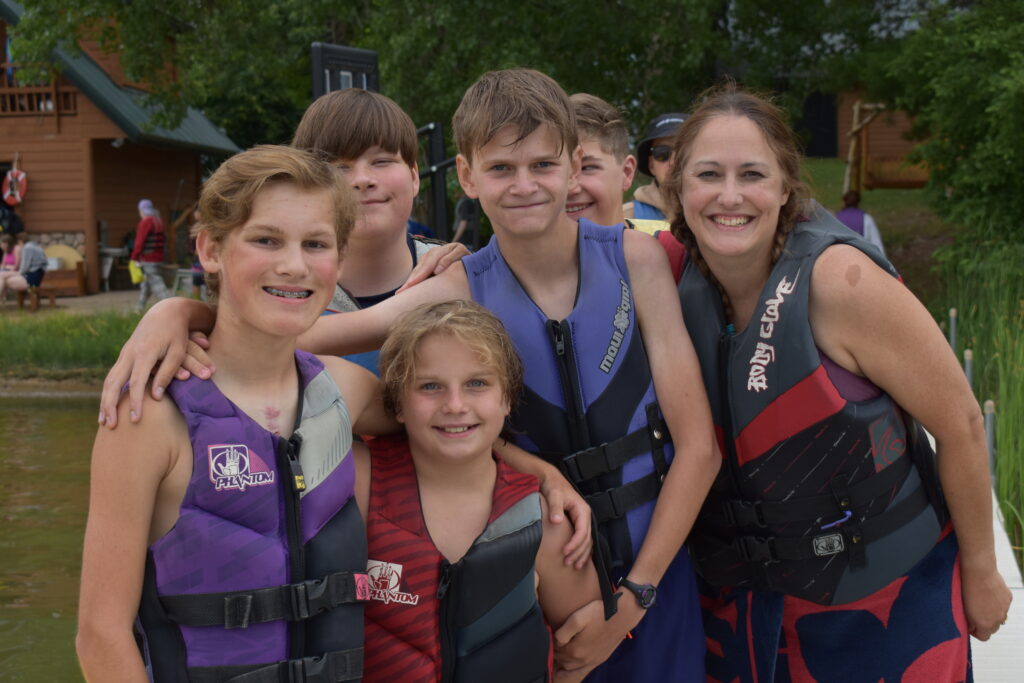 Group of campers and a volunteer wearing lifejackets, standing on the dock