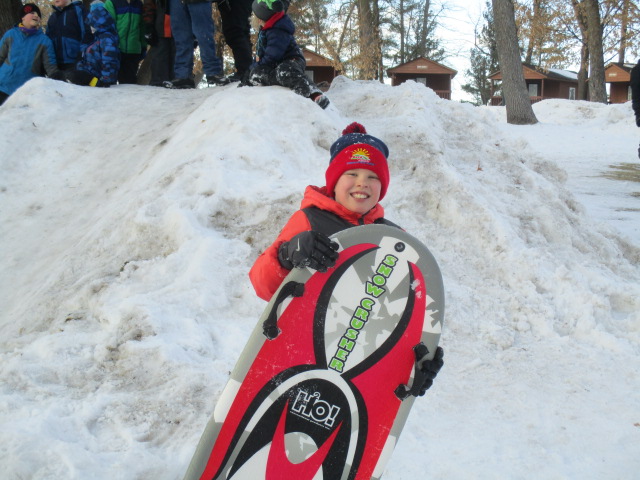 young boy holding sled in front of pile of snow