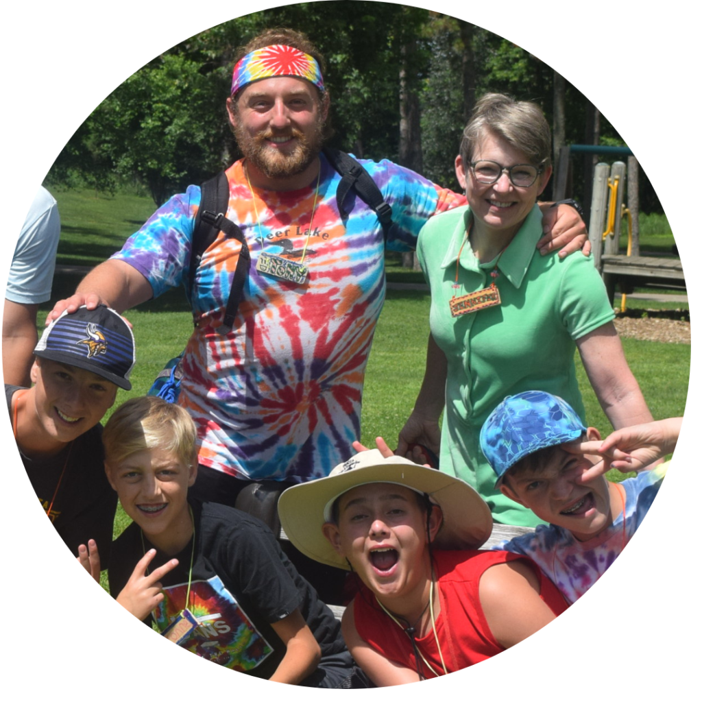 Volunteer counselor in tie dye and nurse in green with four excited campers