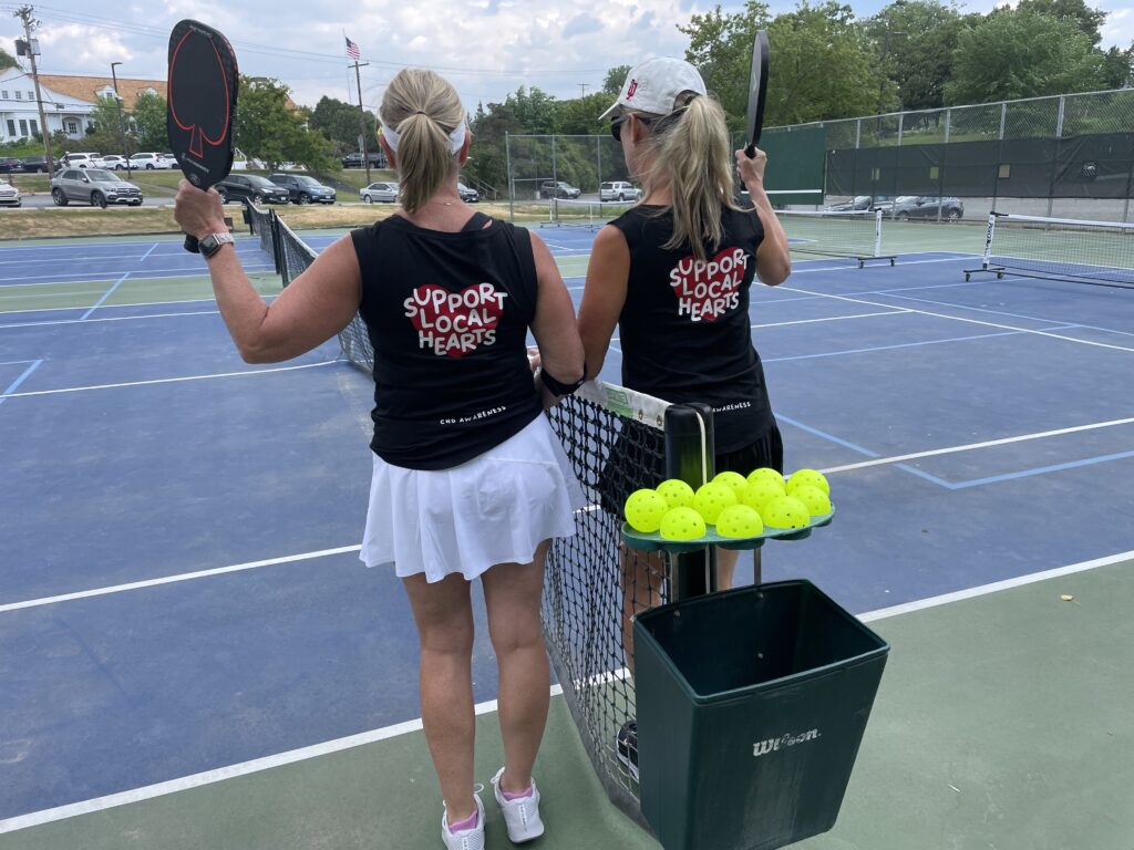 Two pickleball players wearing shirts that say 'support local hearts'