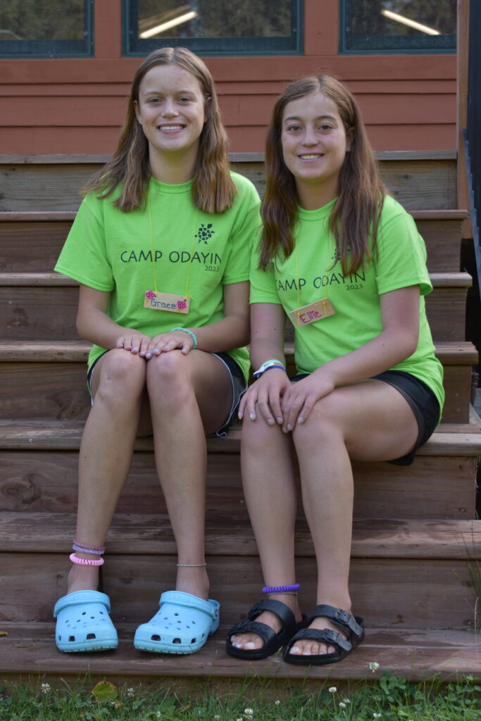 Two campers seated on steps, wearing green Camp Odayin shirts