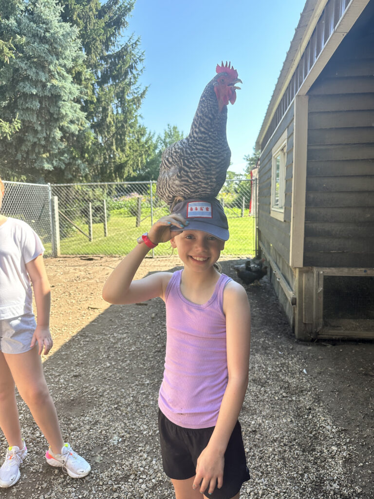 Camper wearing a hat with a rooster perched on their head