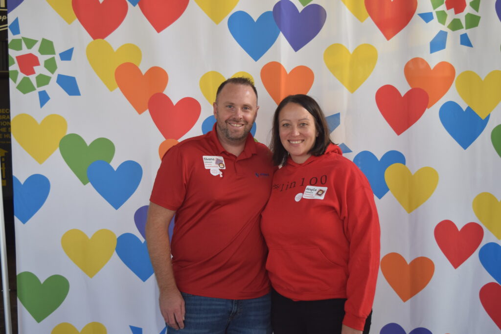 Two guests in red pose in front of heart background