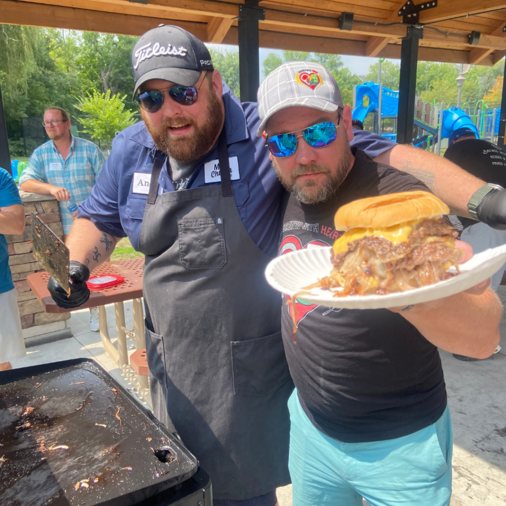 Two dads day participants holding up a burger at a grill