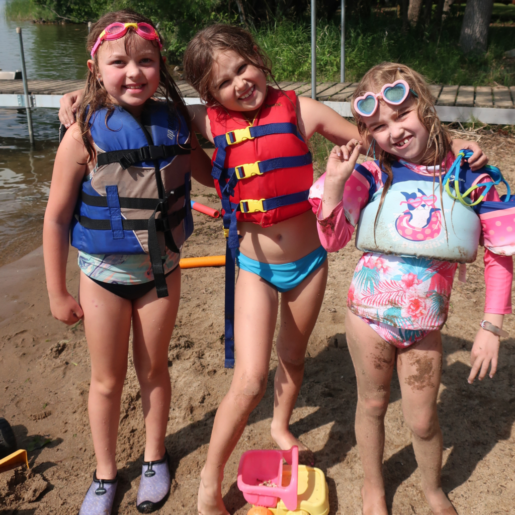 Three campers in swimsuits stand in the sand together