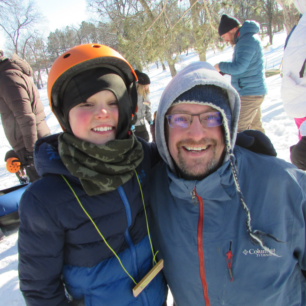 A camper and volunteer smile outside in the snow