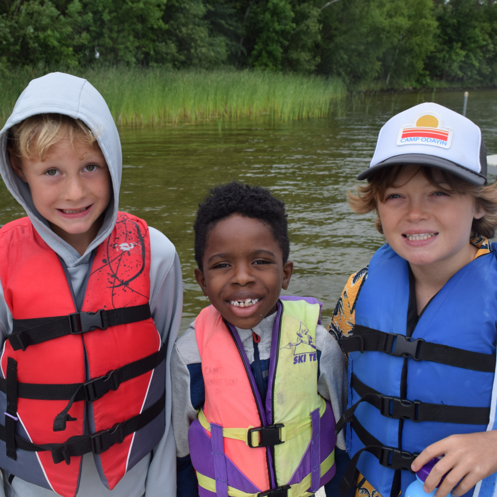 Three campers wearing lifejackets in front of a lake