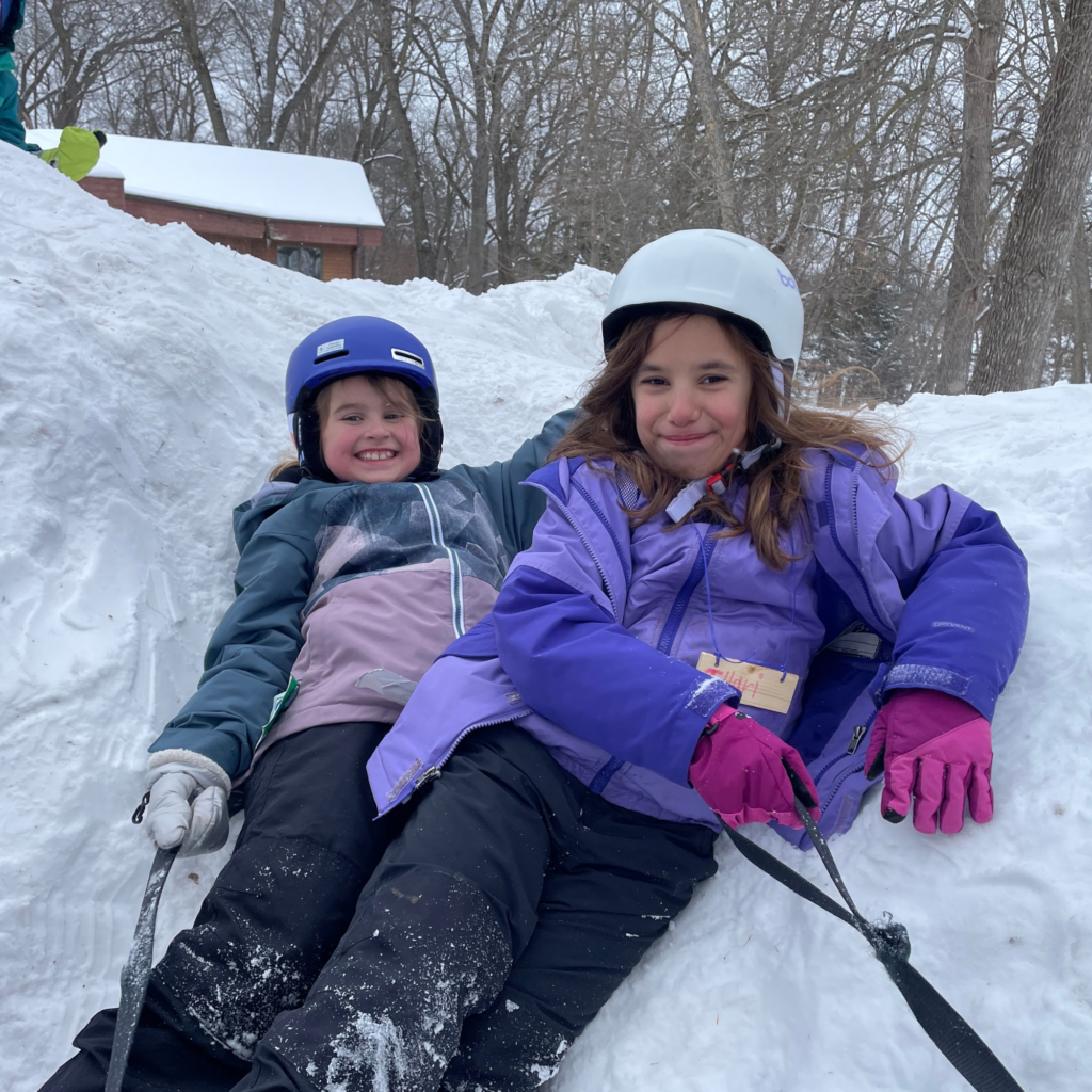 Two campers wearing helmets laying in the snow